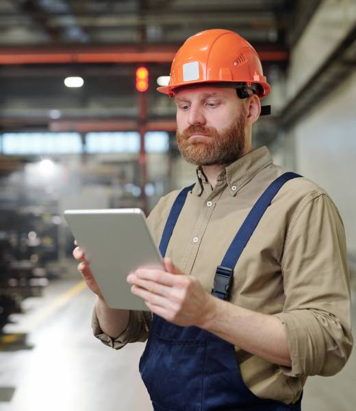 Busy young factory worker in overalls checking work file on tablet while working in industry